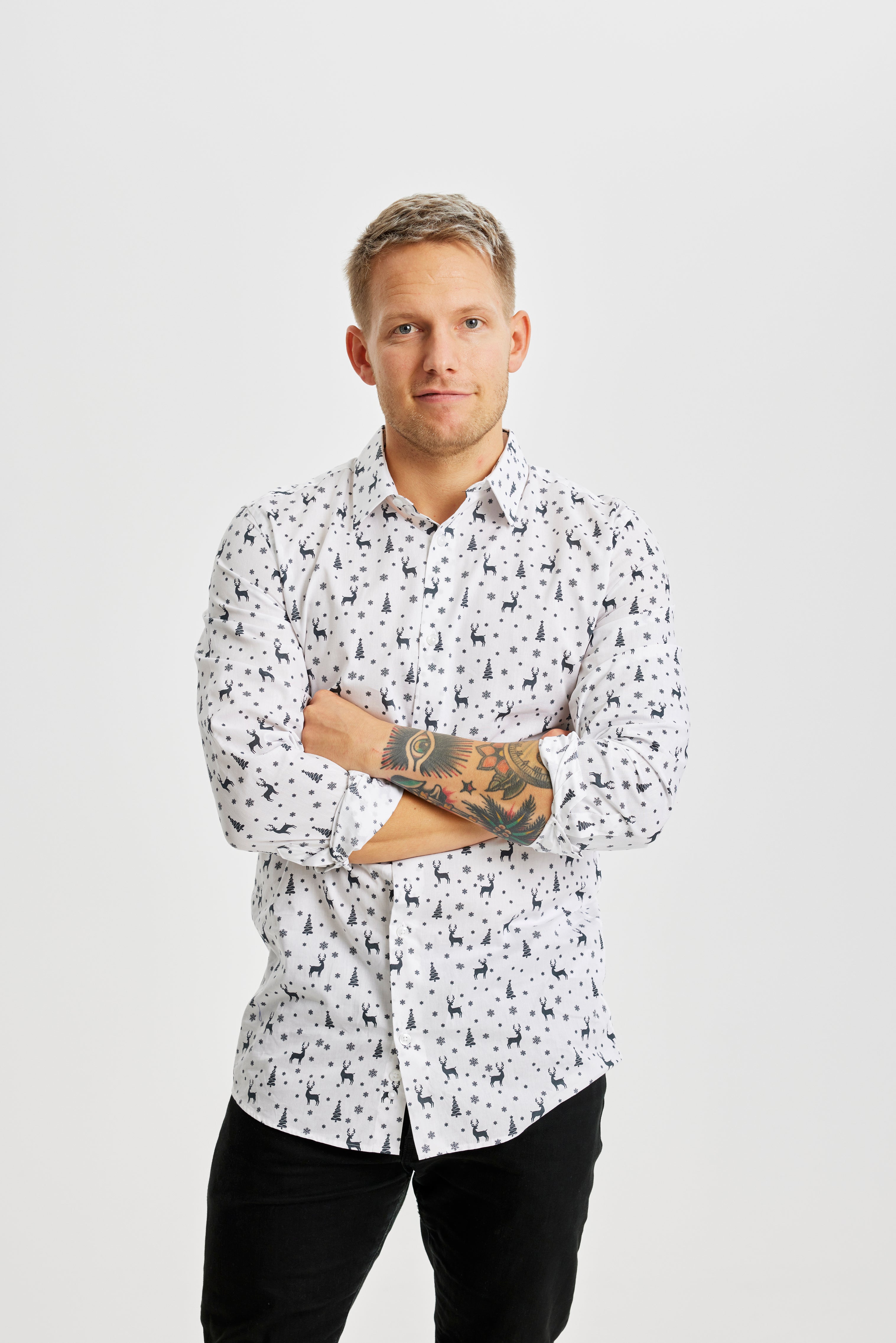 Ein Mann mit verschränkten Armen, der ein weißes Weihnachtshemd mit Weihnachtsmotiv trägt.